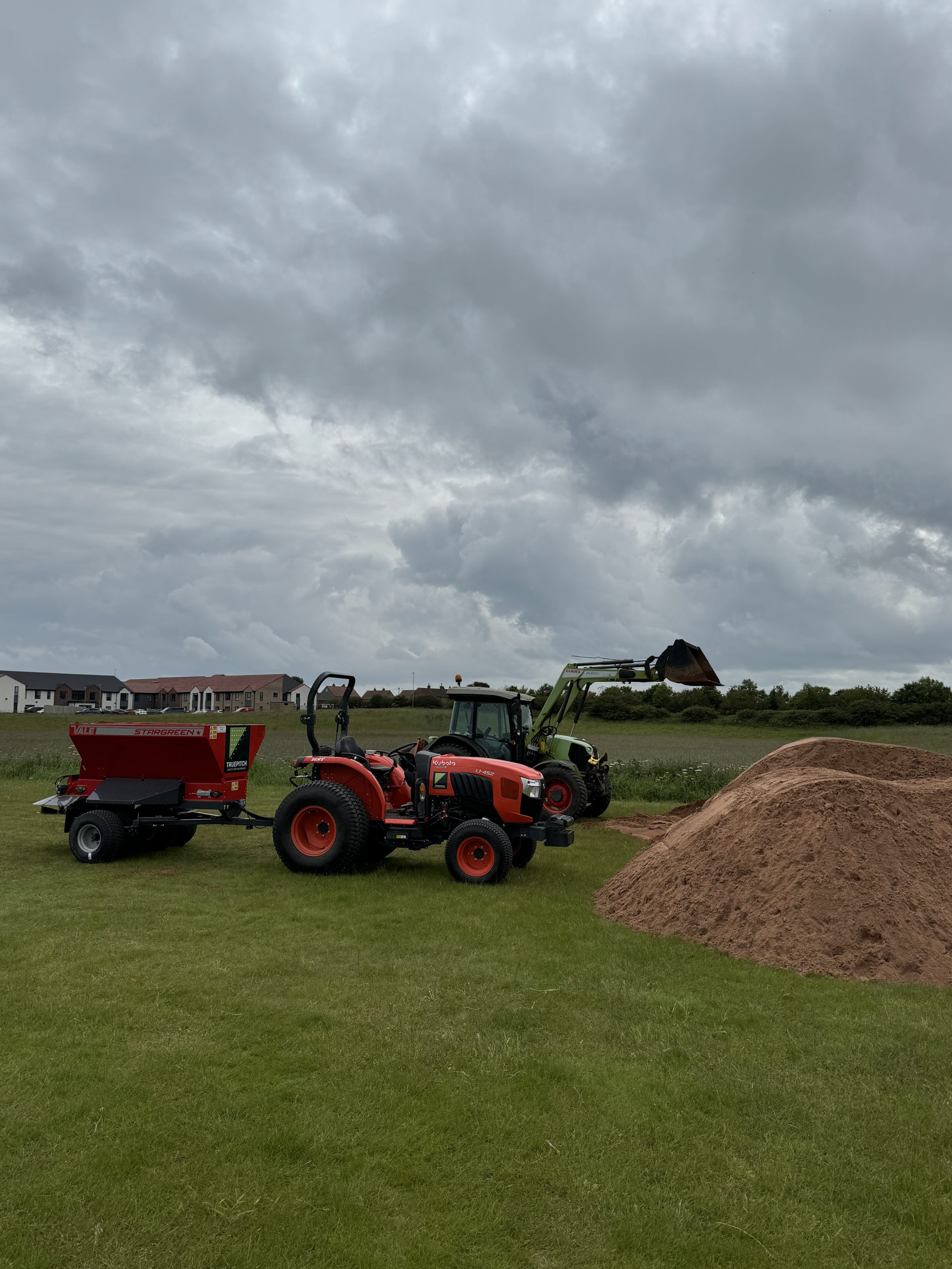 top dress filey 2 Stationary orange tractor pulling a grass disc seeder on a football pitch.